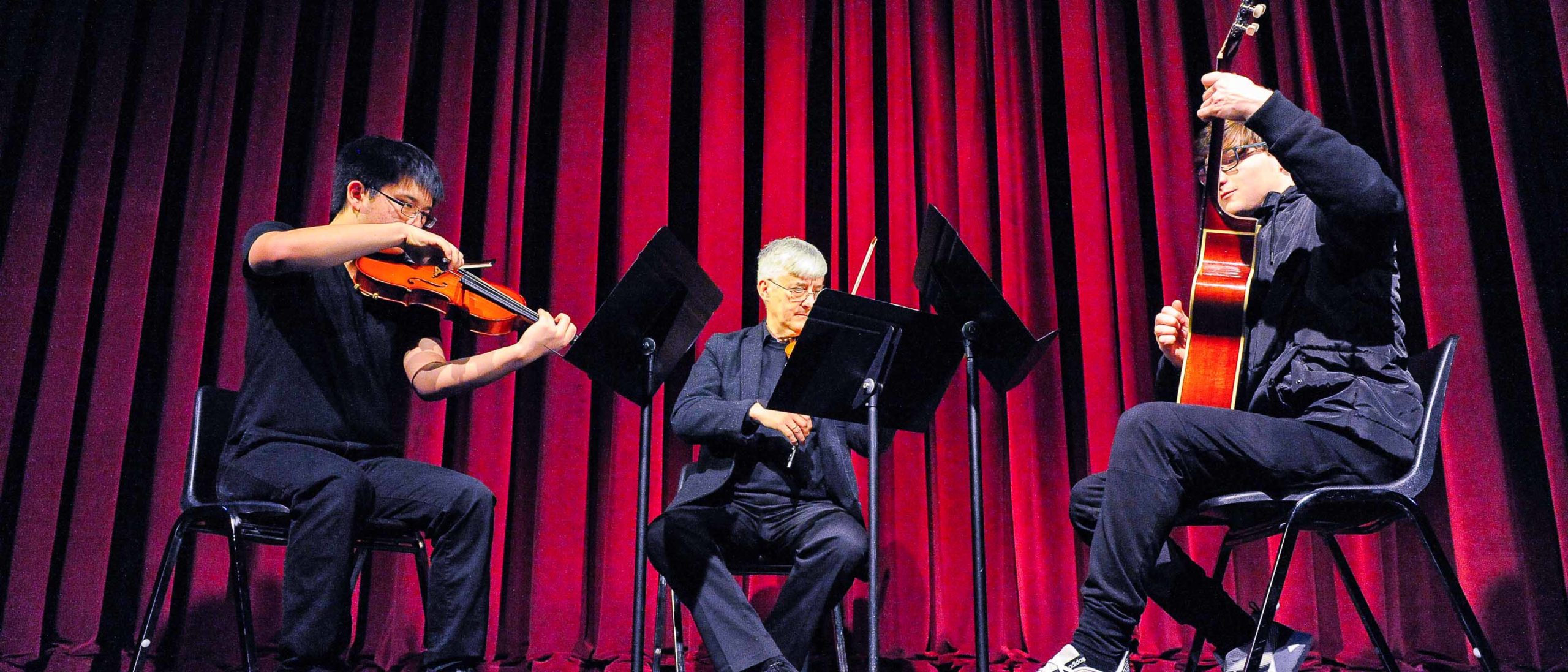 Two students an a faculty member playing string instruments on stage